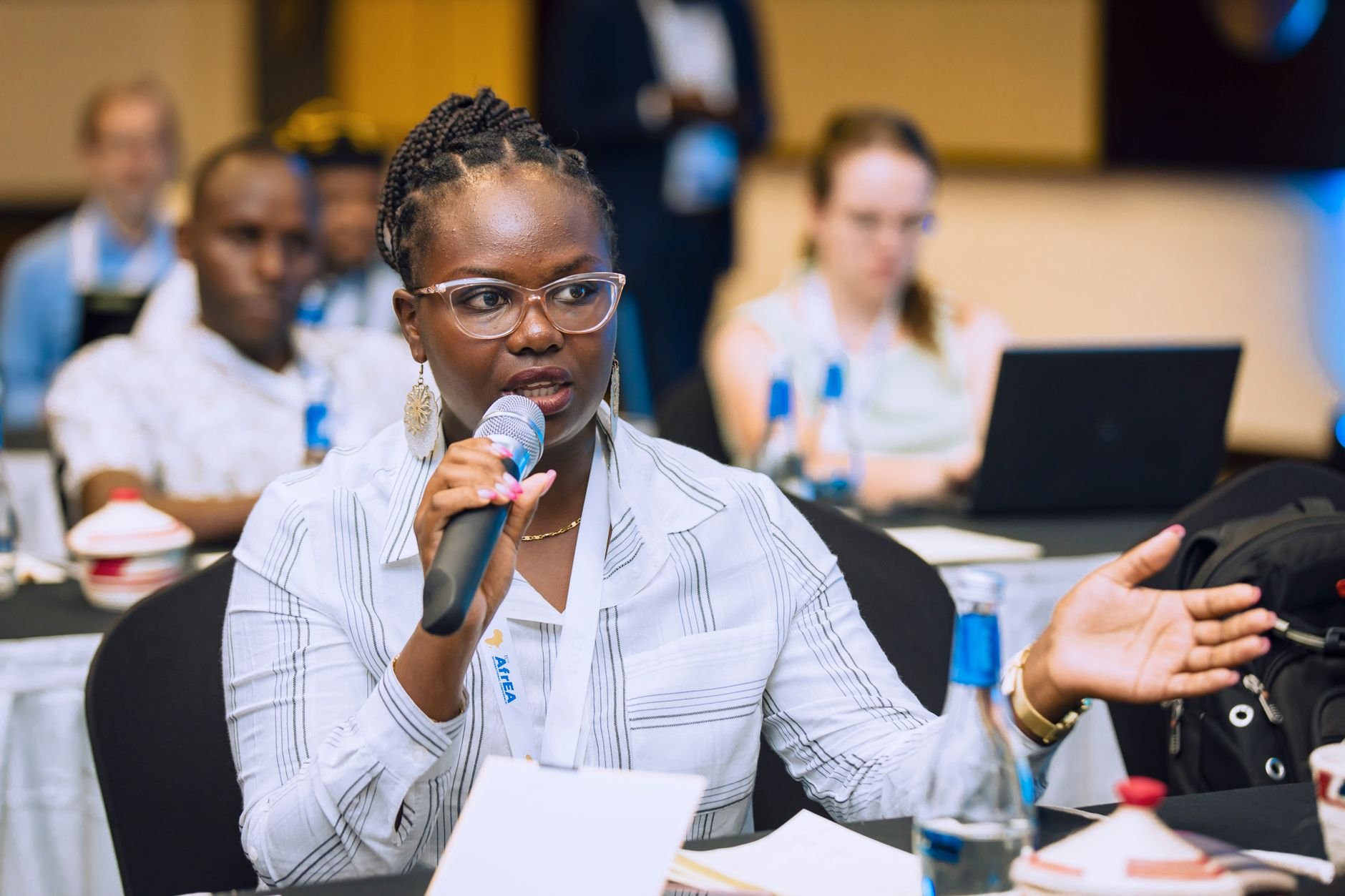 Woman speaking into a microphone during a business conference, engaging with audience.